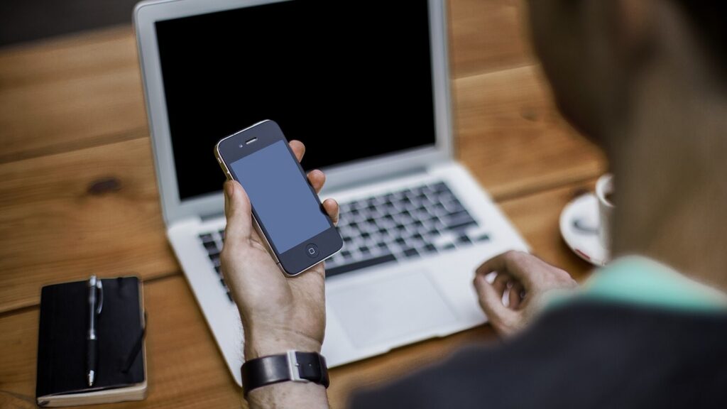 Person using a smartphone beside an open laptop