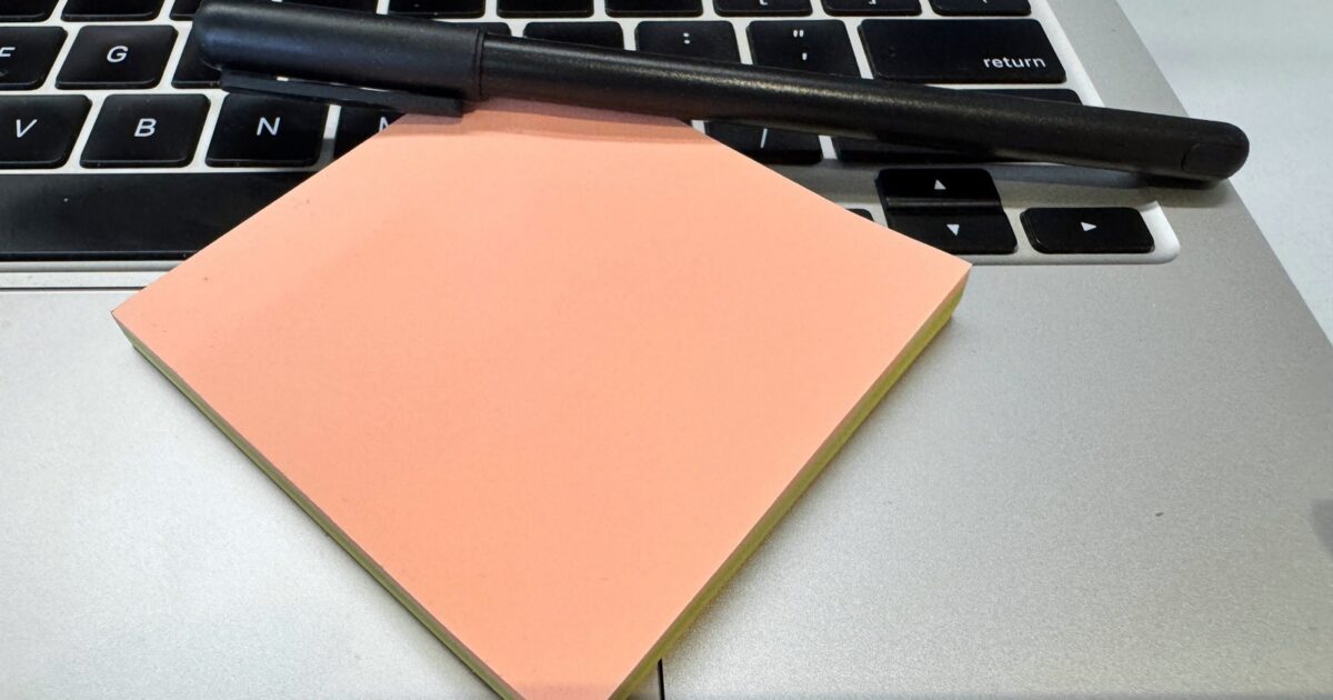Black pen and peach sticky notes rest on a silver laptop keyboard.
