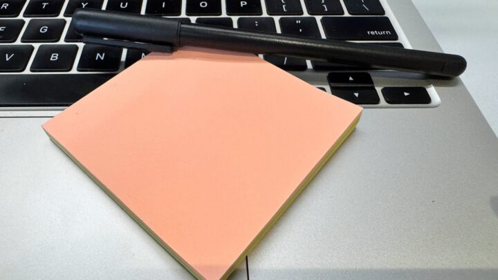 Black pen and peach sticky notes rest on a silver laptop keyboard.