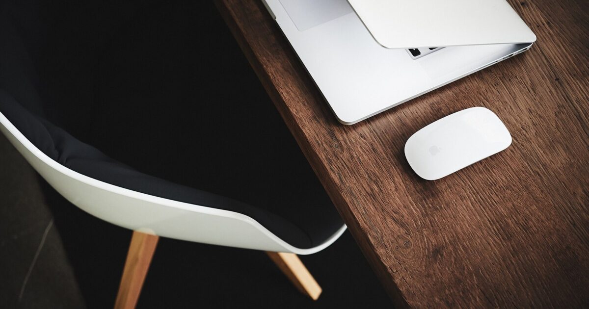 Half-closed laptop and wireless mouse on a wooden desk