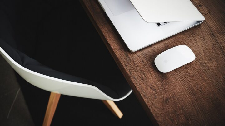 Half-closed laptop and wireless mouse on a wooden desk