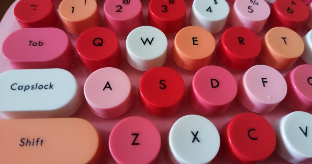 A close-up view of a colorful keyboard featuring round, brightly colored keycaps in shades of pink, red, and white.