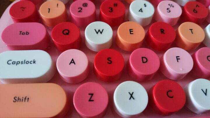 A close-up view of a colorful keyboard featuring round, brightly colored keycaps in shades of pink, red, and white.
