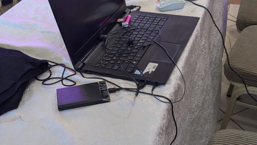 A table covered with a white lace cloth displays three open laptops, not powered on, one is alongside a portable battery pack and a computer mouse.