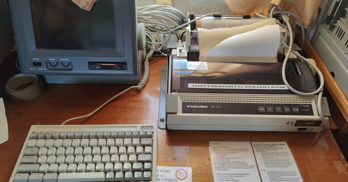 A vintage ship communication setup with a CRT monitor, keyboard, and printer, along with printed instructions, likely for maritime navigation and communication.