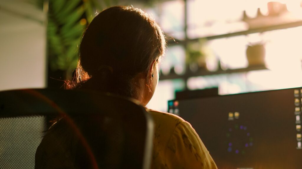 A girl working on a computer system near a window with sunlight is shining through it.