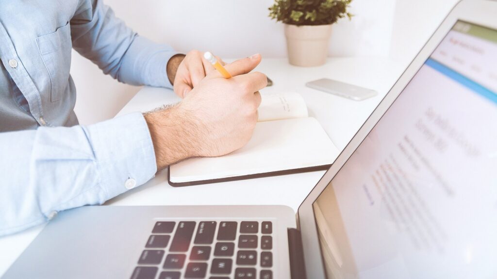 Person working at a desk with a laptop and notebook.