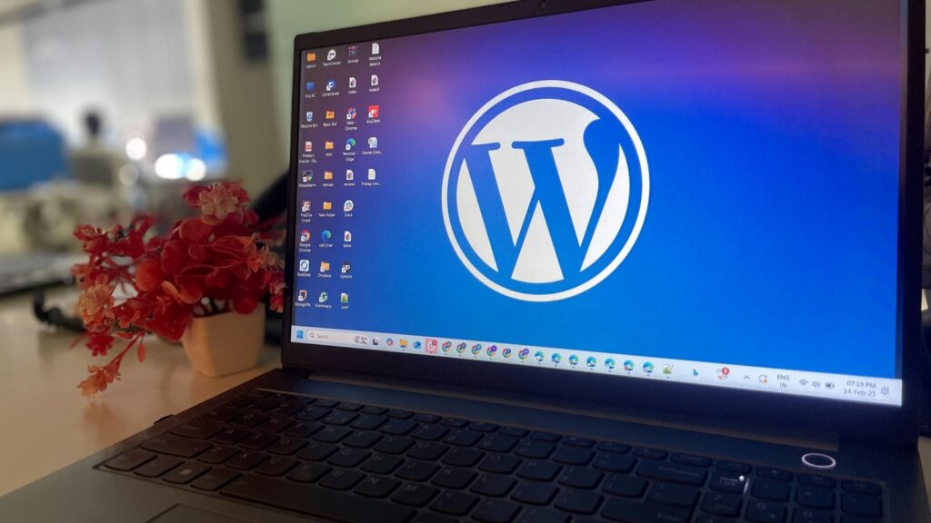 A laptop on a desk with a large WordPress logo displayed on the screen.