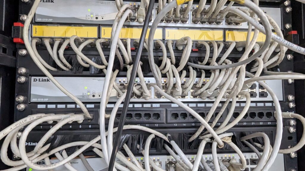 A messy network server room showing wires, patch panels in a room
