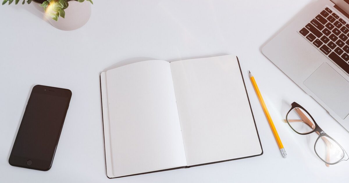 Smartphone, laptop, notebook, pencil, and glasses arranged on a clean desk