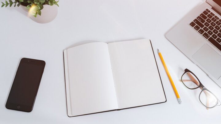 Smartphone, laptop, notebook, pencil, and glasses arranged on a clean desk