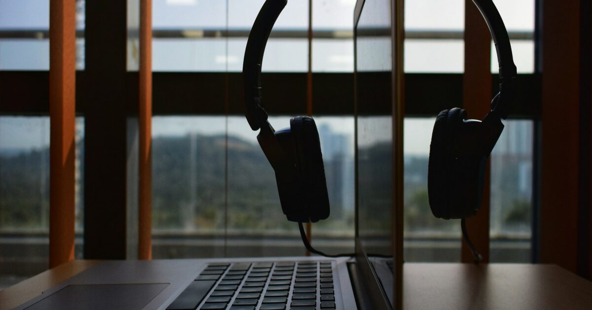A work desk in a city office with a macbook air and a headset hanging over the screen.