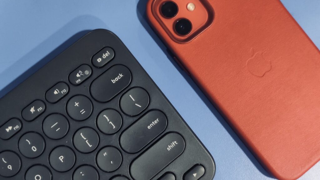 Partial view of a black keyboard beside a red iPhone on a blue surface