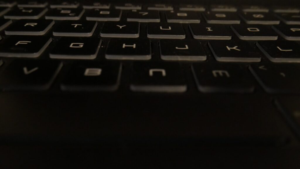 A close-up view of a black laptop keyboard, focusing on the keys with visible wear and dust.