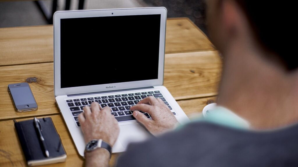 Person typing on a laptop at a wooden desk.