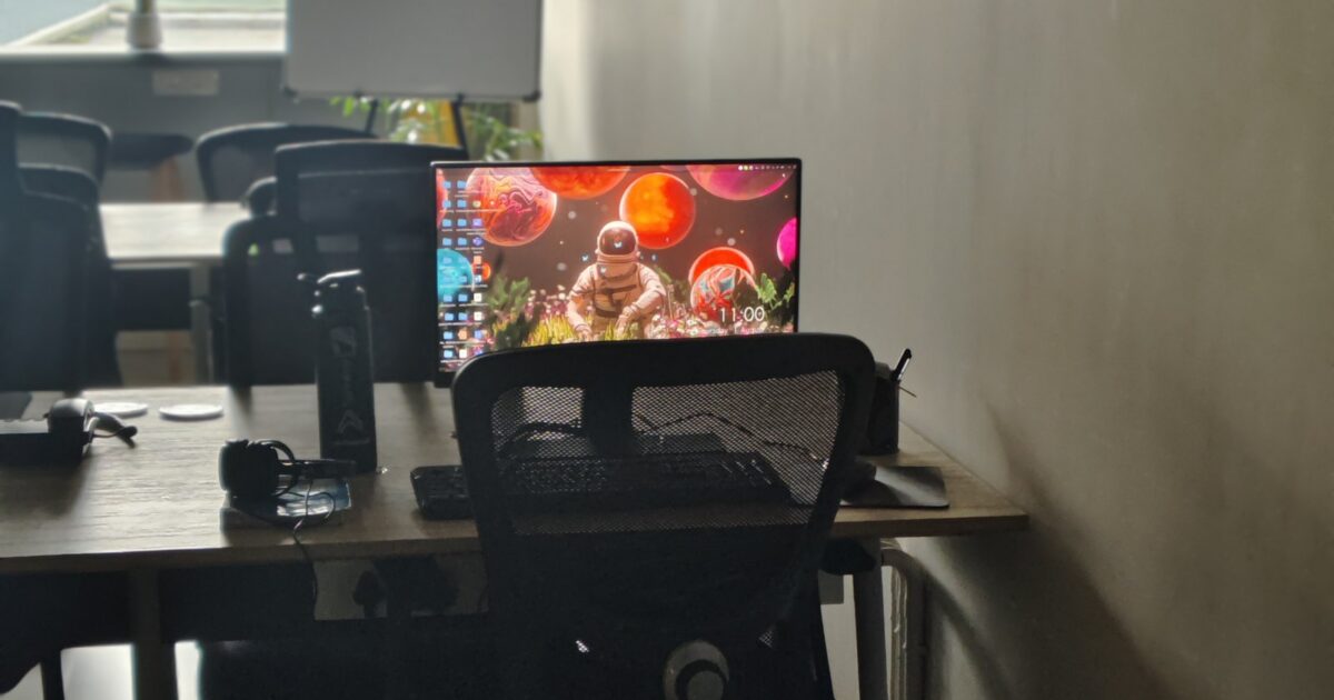 Bright computer screen on a table in a drab room full of other tables.