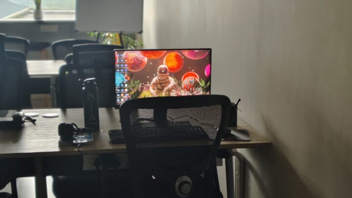 Bright computer screen on a table in a drab room full of other tables.