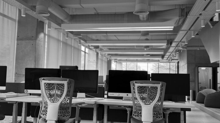 A modern office space featuring several white desks with computer monitors and ergonomic chairs.