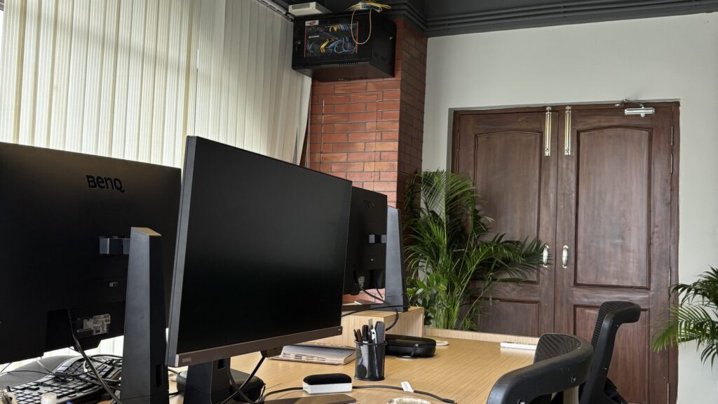 A modern office space with a long wooden desk featuring two black monitors.