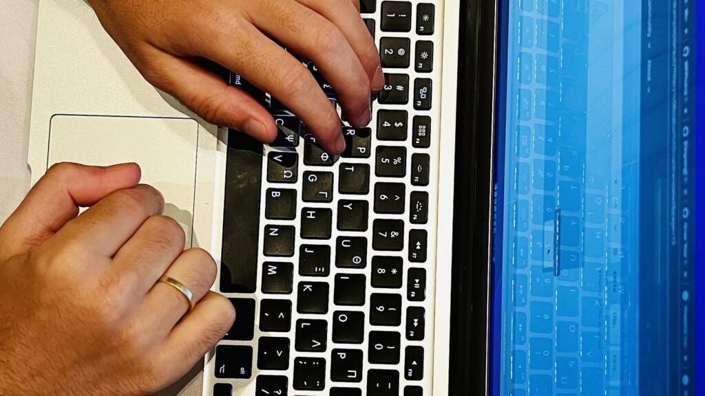 Typing on a laptop with phone by the side