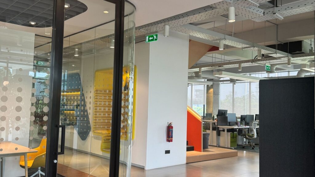 Modern office with glass-walled meeting room featuring yellow chairs.