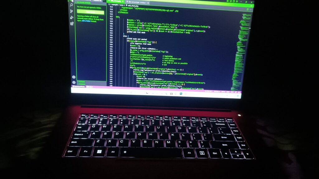 A laptop with illuminated keyboard and green texts on the screen in a dark room.