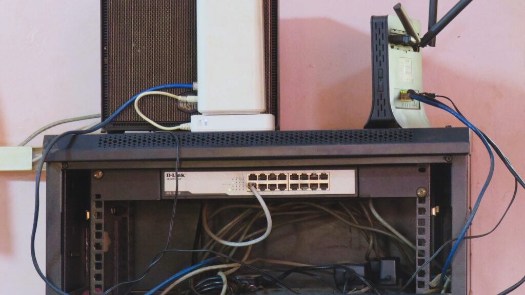 A front-facing shot of a black wall-mounted network rack containing a 16-port network switch with several connected Ethernet cables.